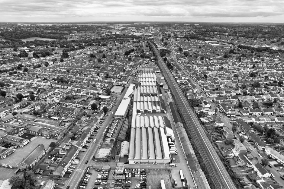 A black and white aerial photograph of Watford junction station showing railway tracks, platforms, and a train in the station yard. Surrounding the station are tall modern office buildings, smaller co